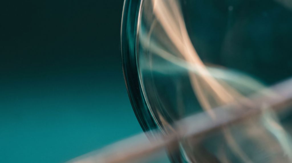 Lente óptica sobre fundo petróleo, com feixe de luz atravessando.